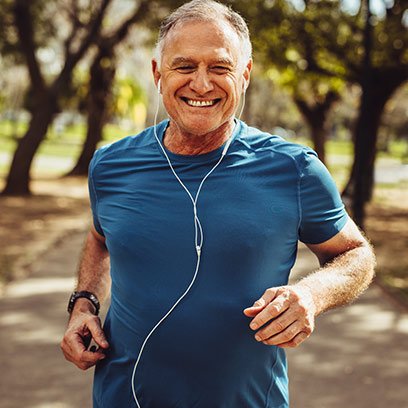 elderly man wearing blue t-shirt running at the park while wearing earphones and watch
