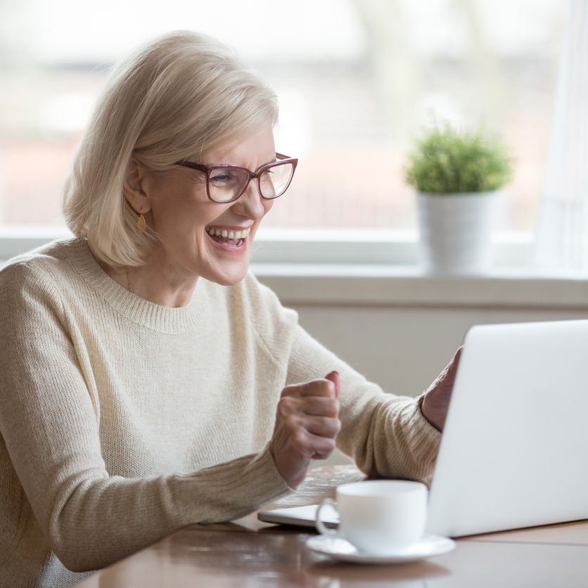 elderly woman enjoying a coffee while working on a laptop